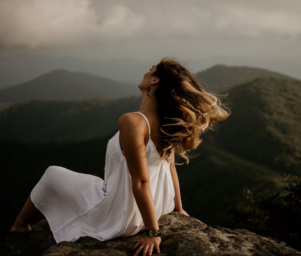 Frau mit weißen Kleid sitzt auf einem Berg, Unplash